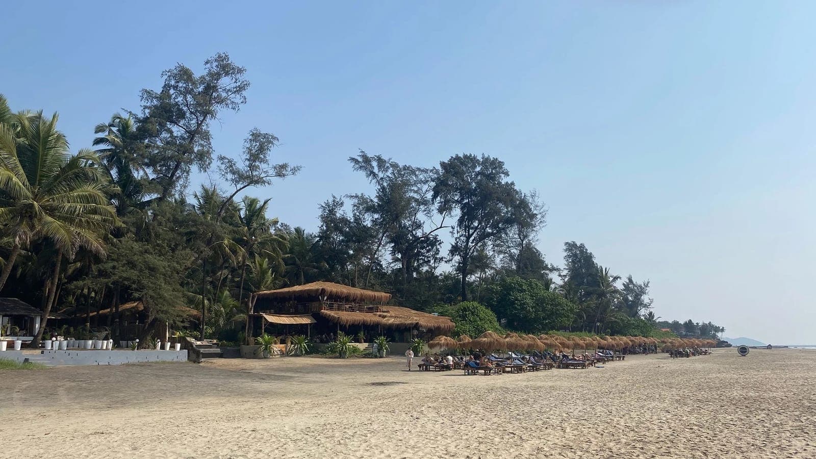 A long, quiet stretch of Mandrem Beach with a simple beach shack and empty sand