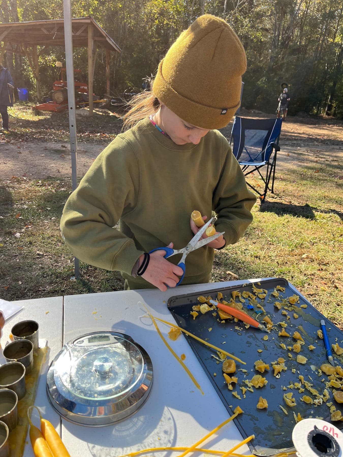 A child cutting beeswax with scissors at an outdoor candle-making table