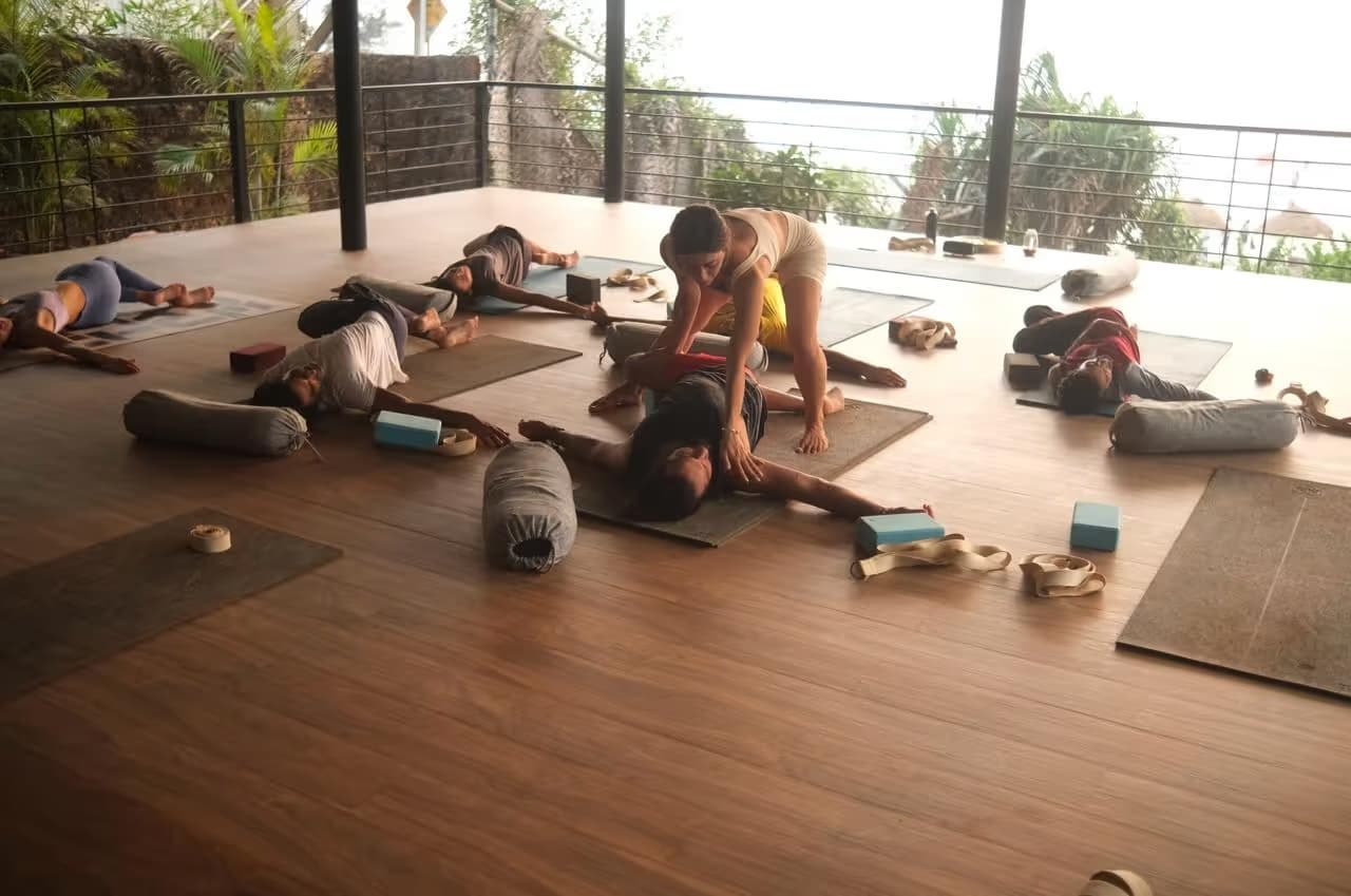 An open-air yoga class on a covered deck surrounded by palms